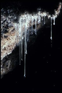 icicles hanging from the side of a rock in the dark, with water running down it