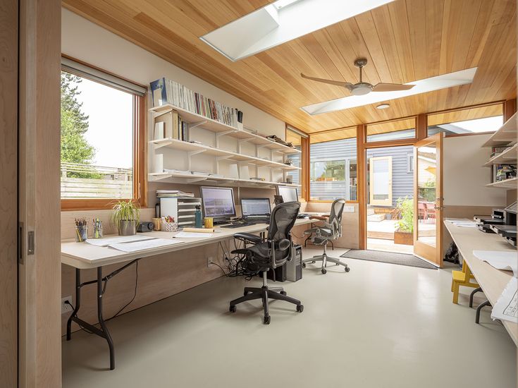 an office with two desks and open shelves on the wall, along with a ceiling fan