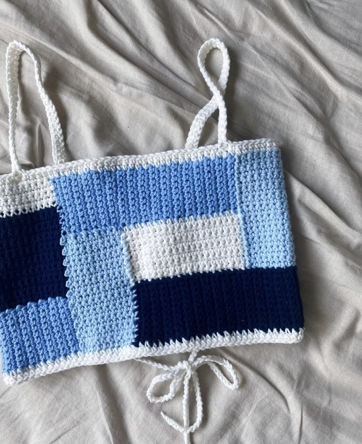 a crocheted blue and white bag laying on top of a bed next to a pillow