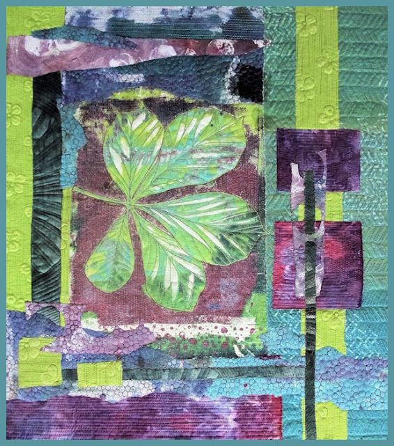 a green leaf is on top of purple and green fabric, with squares in the background