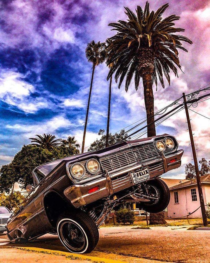 an old car is parked on the side of the road in front of a palm tree