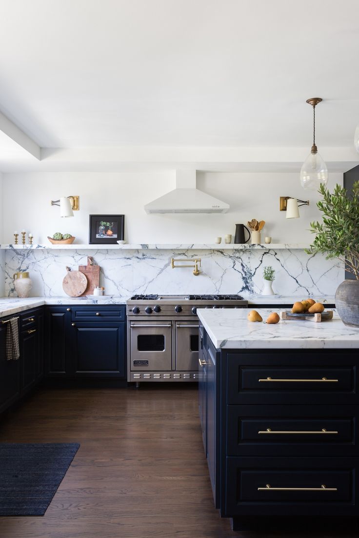 a kitchen with marble counter tops and black cabinets, along with brass pulls on the doors