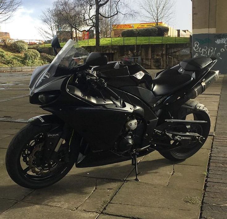 a black motorcycle parked on the side of a road next to a wall with graffiti