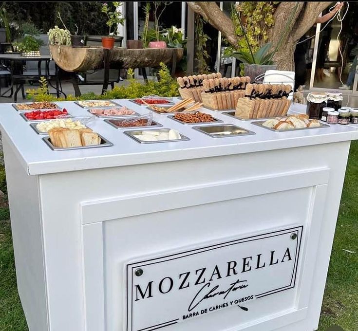 a table that has some food on top of it in front of a tree and grass area