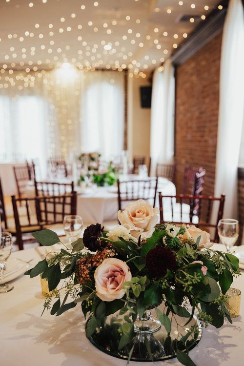 an arrangement of flowers in a glass vase on a table with white linens and lights