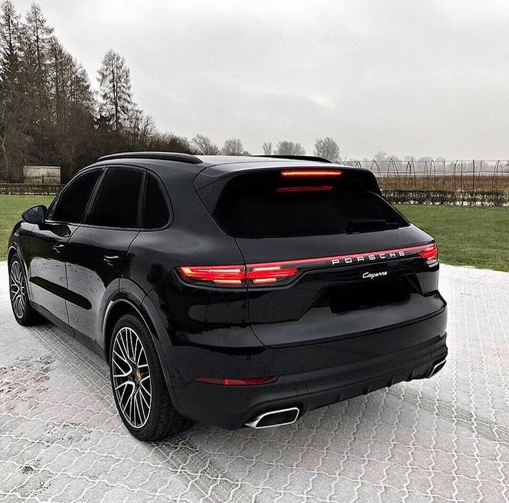 the rear end of a black porsche cayenne parked in front of a field