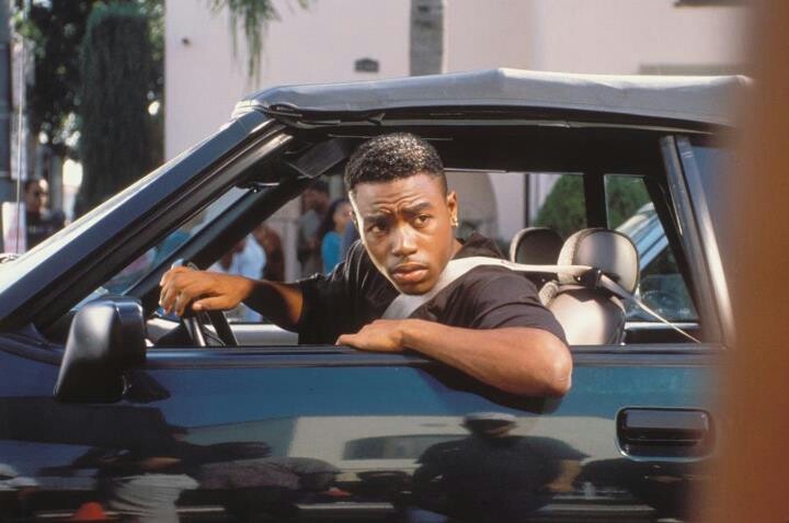 a man sitting in the driver's seat of a blue car with his hand on the steering wheel