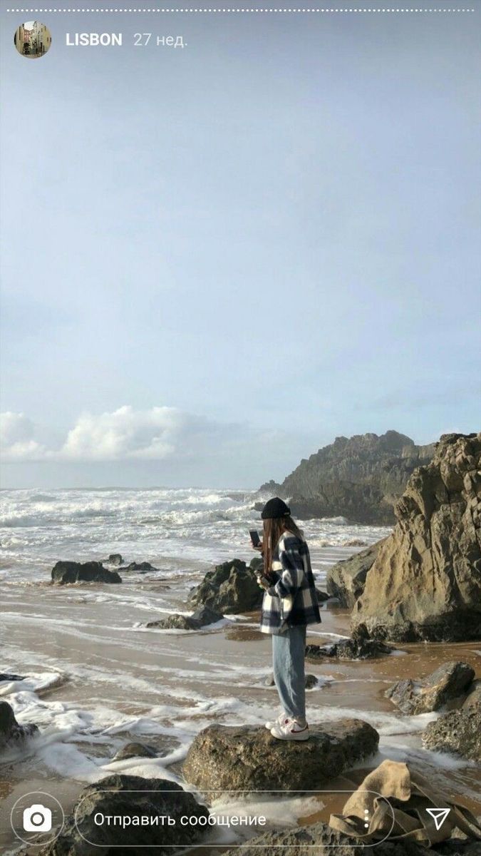 a person standing on some rocks near the ocean and holding an object in their hand