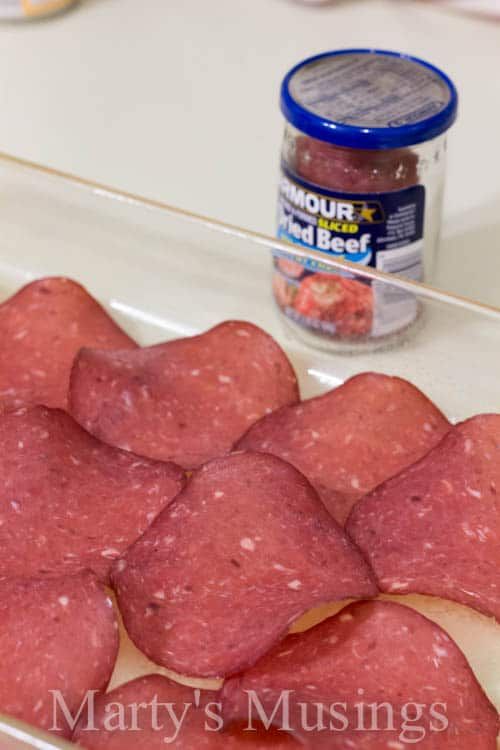 raw meats are sitting on a counter next to a jar of mustard