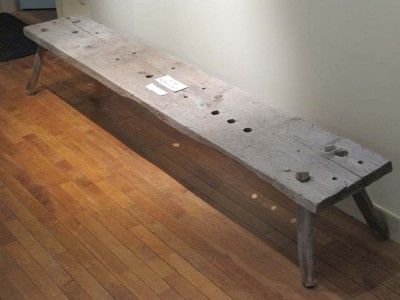 a wooden bench sitting on top of a hard wood floor next to a white wall