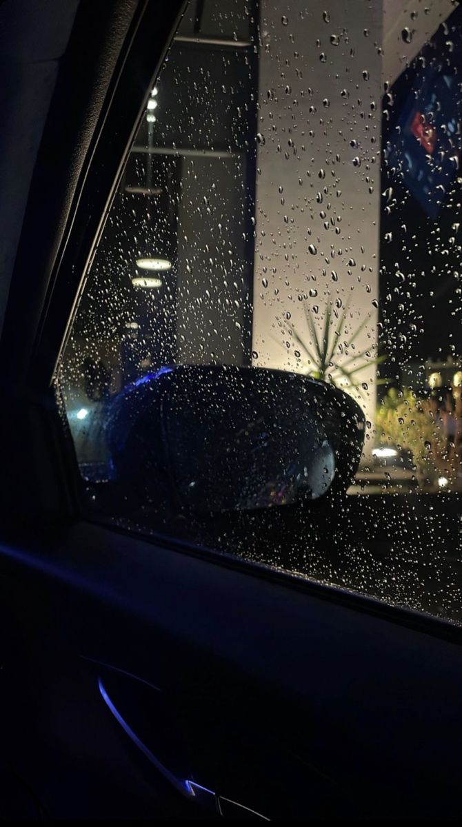 rain drops on the windshield of a car in front of a tall building at night