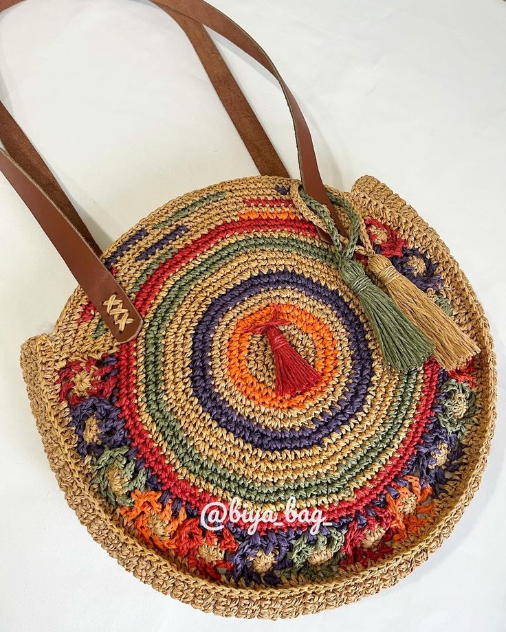 a multicolored straw bag with tassels and leather handles on a white surface