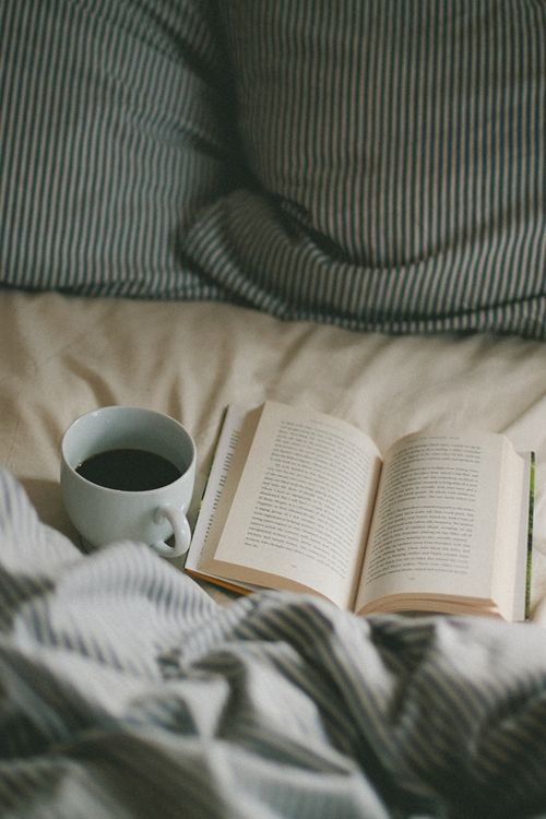 an open book sitting on top of a bed next to a cup of coffee