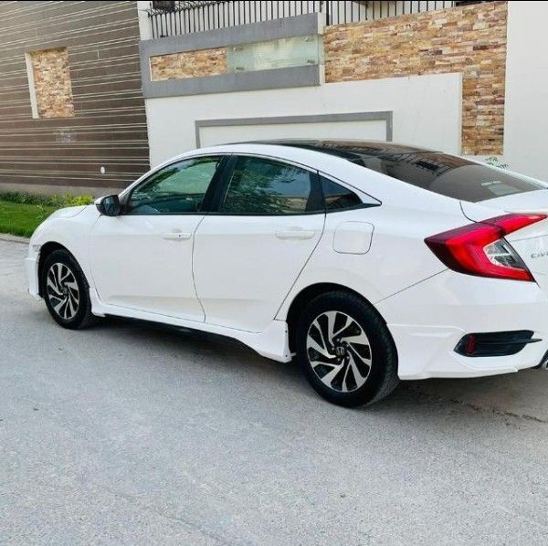 a white honda civic parked in front of a building with brick walls and garage doors