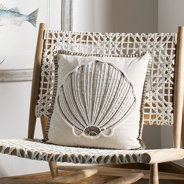 a white pillow with a shell on it sitting on a wicker chair next to a window