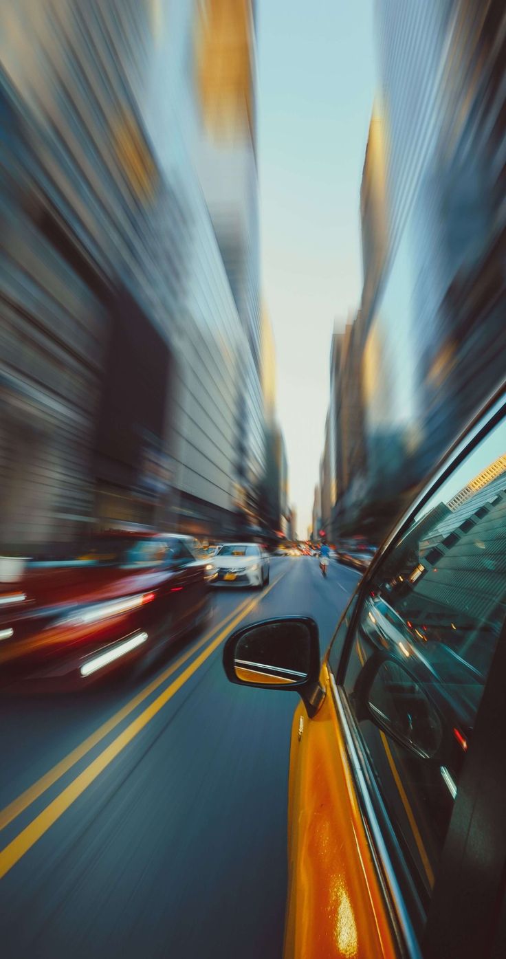 a car driving down a city street with tall buildings in the backgroung