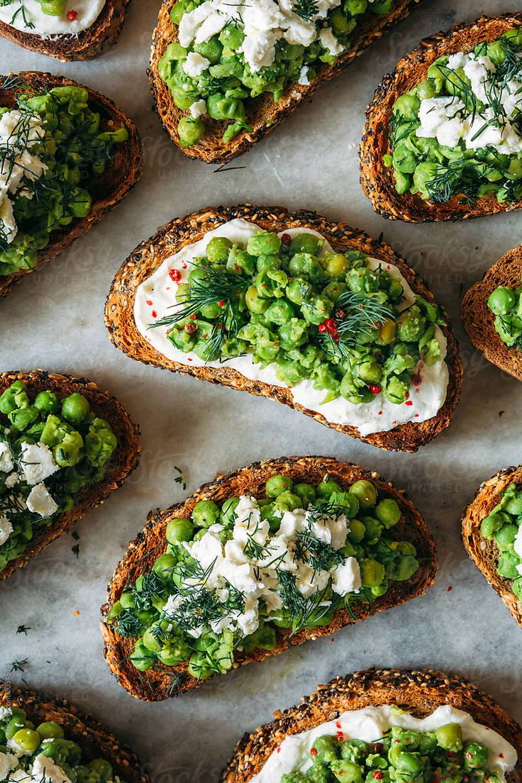 several pieces of bread topped with peas and cream cheese on top of a white surface