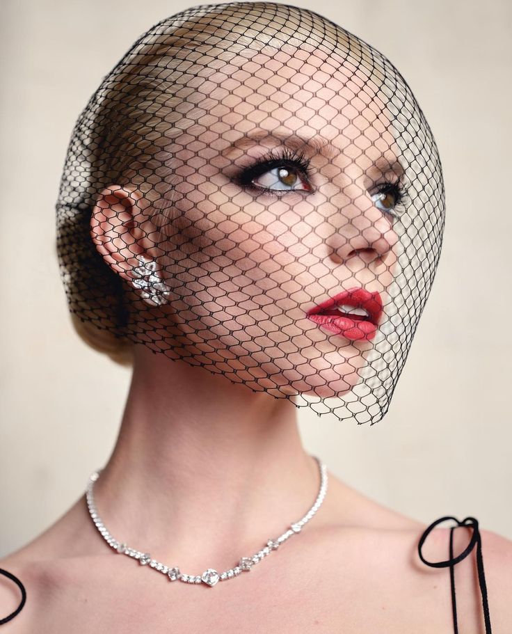 a woman wearing a birdcage veil over her head and holding a diamond necklace