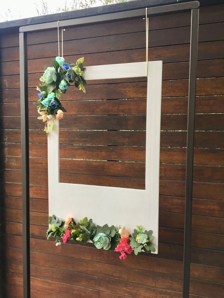 a wooden fence with flowers hanging from it's sides and a white frame on the wall