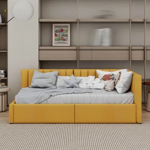 a yellow daybed with pillows on it in front of a bookshelf and shelves