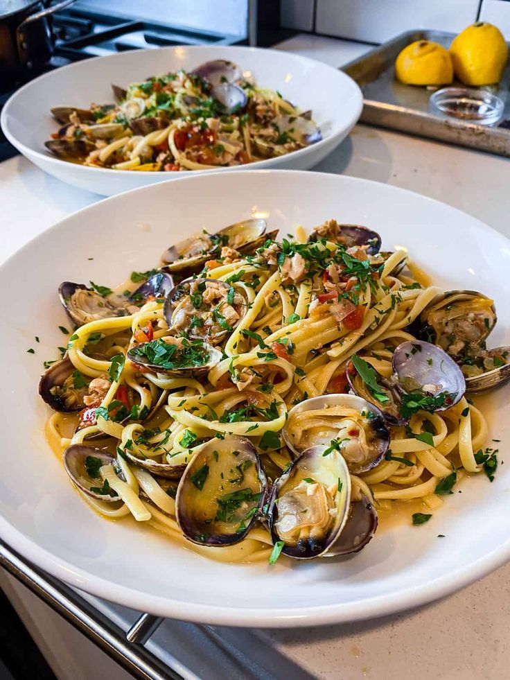 two plates of pasta with clams and lemons on the side, sitting on a kitchen counter