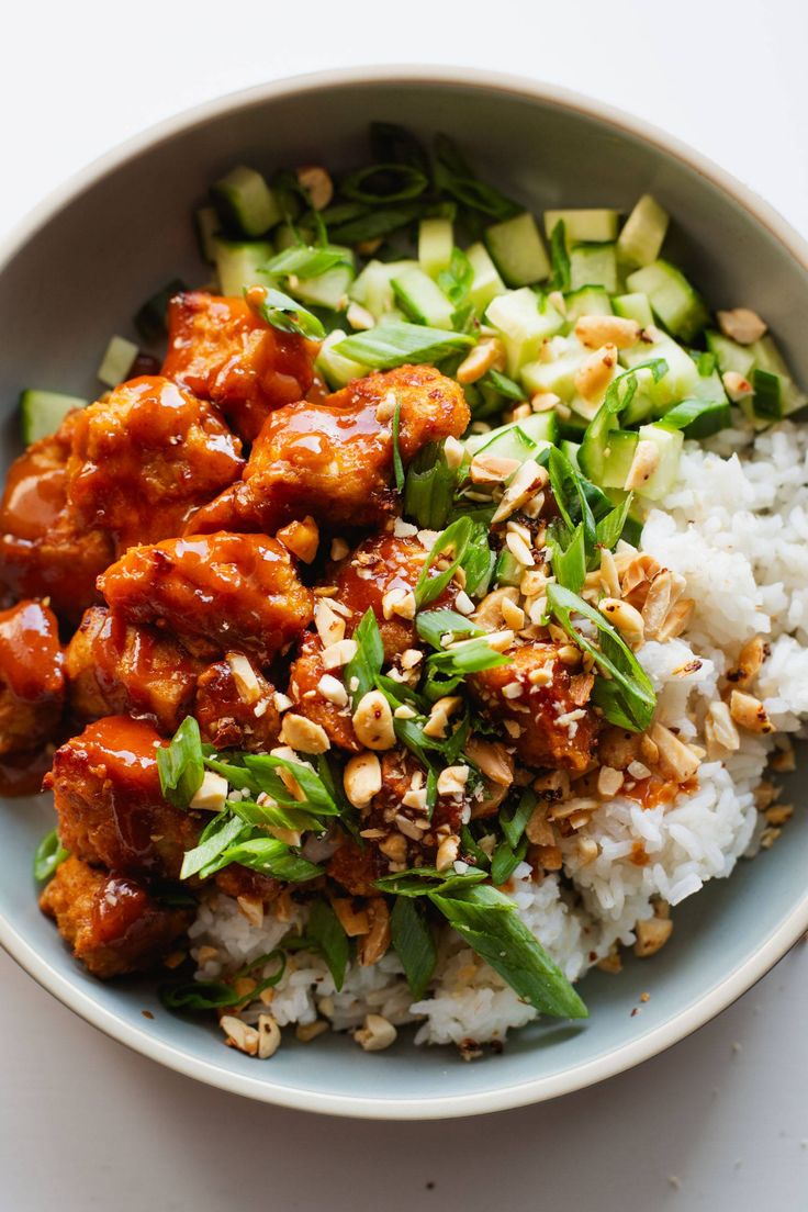 a bowl filled with rice, meat and veggies next to cucumbers