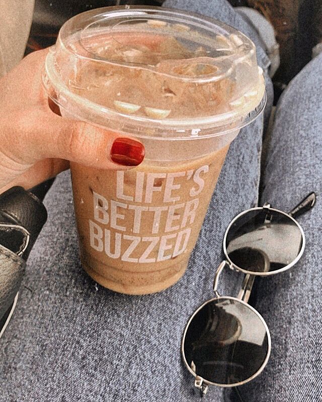 a cup of coffee sitting on top of a person's lap next to sunglasses