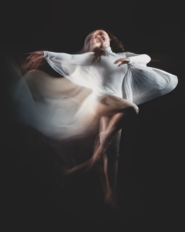 a woman is dancing in the dark with her arms spread out and she's wearing a white dress