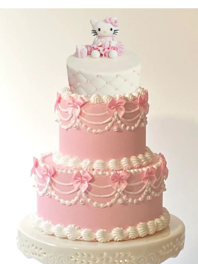 a pink and white three tiered cake with hello kitty on top