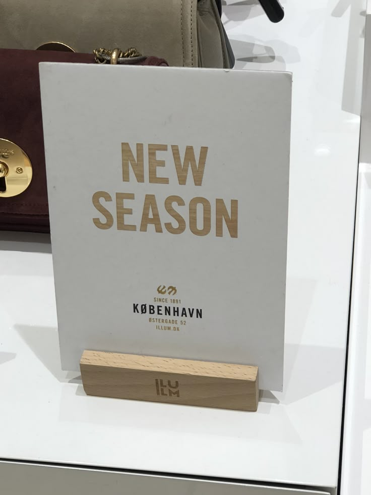 a new season sign on display in a store window with other purses and handbags behind it