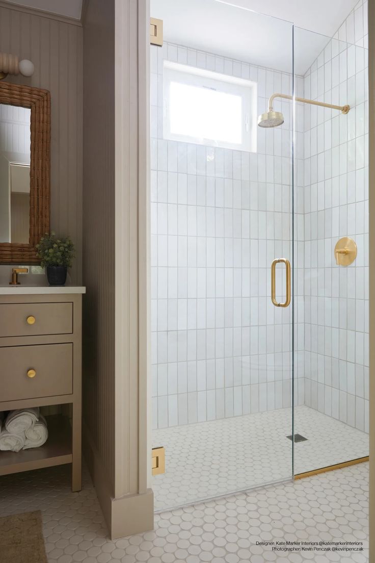 a bathroom with a walk in shower next to a white sink and wooden cabinet under a window