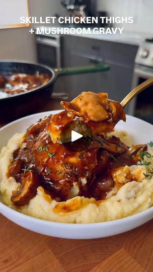 a white bowl filled with mashed potatoes and meat covered in sauce on top of a wooden table