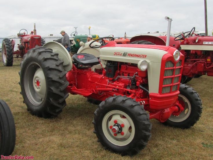 an old red and white tractor parked on top of a grass covered field next to other farm equipment