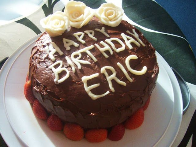 a birthday cake with chocolate frosting and strawberries on a white plate that says happy birthday eric