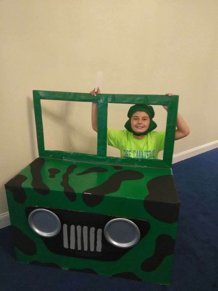 a young boy dressed as a green camo truck with his hands in the window