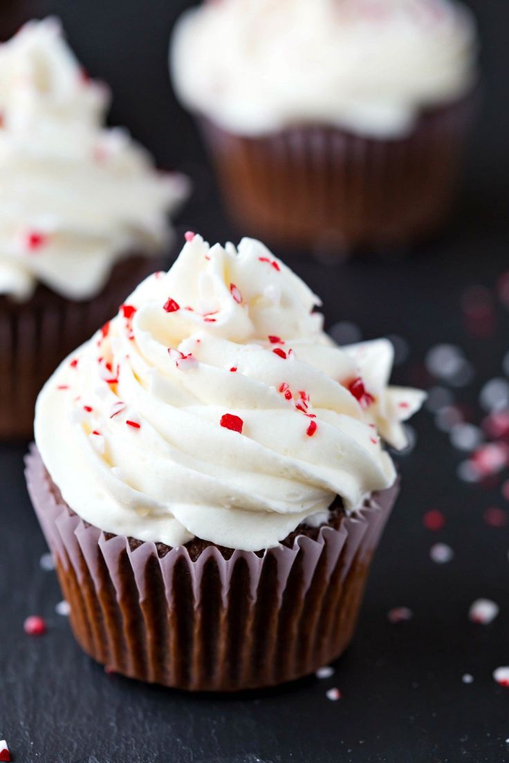 cupcakes with white frosting and sprinkles on a black surface