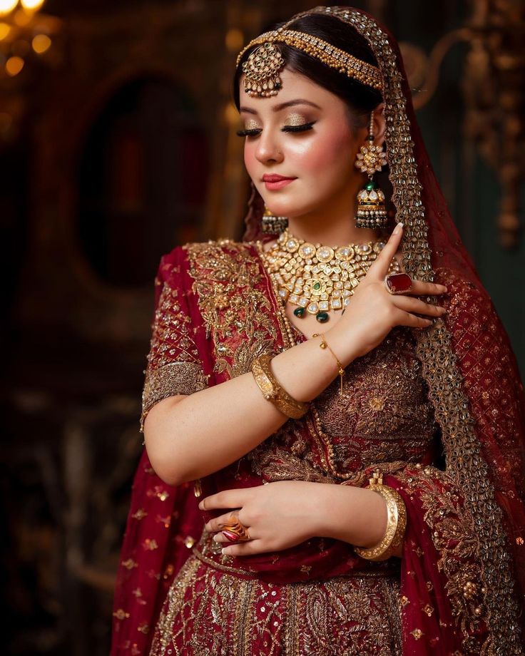 a woman in a red and gold bridal outfit with her hands on her chest