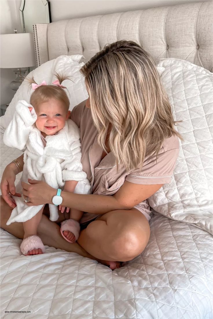 a woman holding a baby in her arms on top of a bed with white sheets