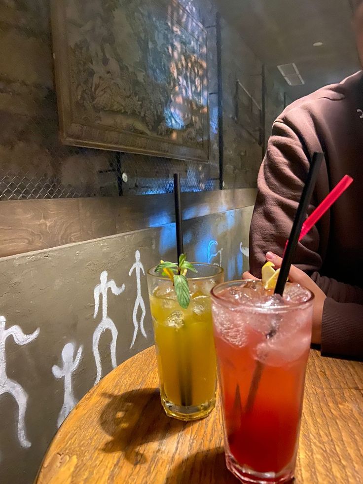 two drinks sitting on top of a wooden table next to each other in front of a man