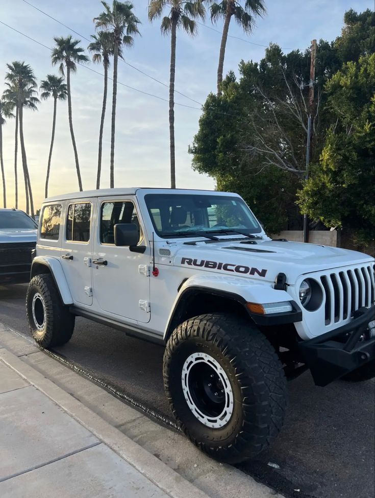 a white jeep is parked on the side of the road with palm trees in the background