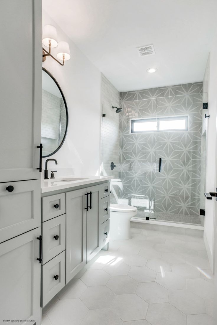 a white bathroom with gray and white wallpaper, tile flooring and large mirror