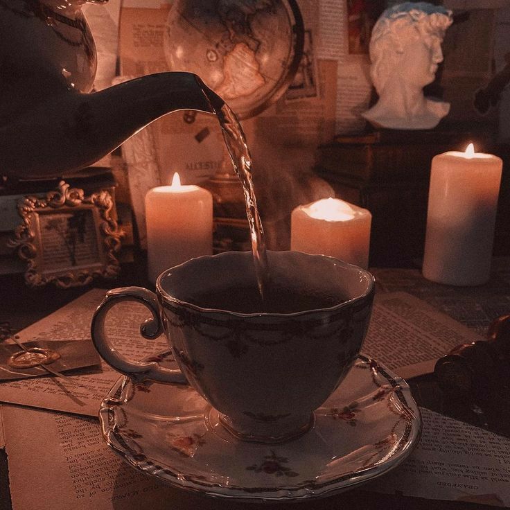 a teacup filled with liquid sitting on top of a table next to some candles