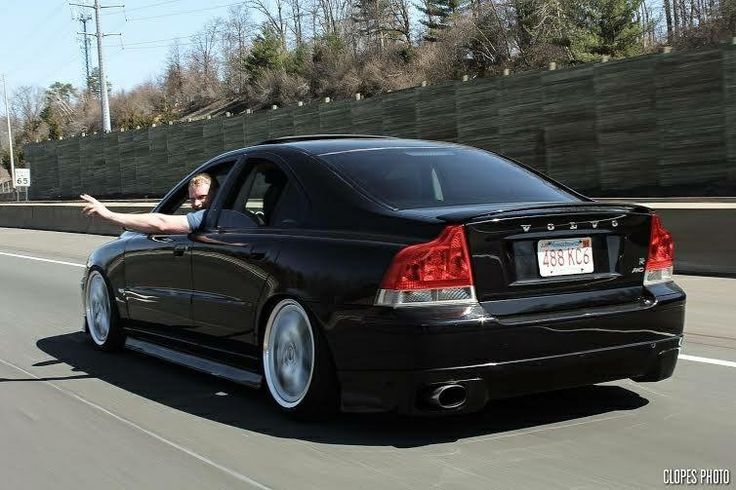 a man leaning on the back of a black car while pointing at something in the distance