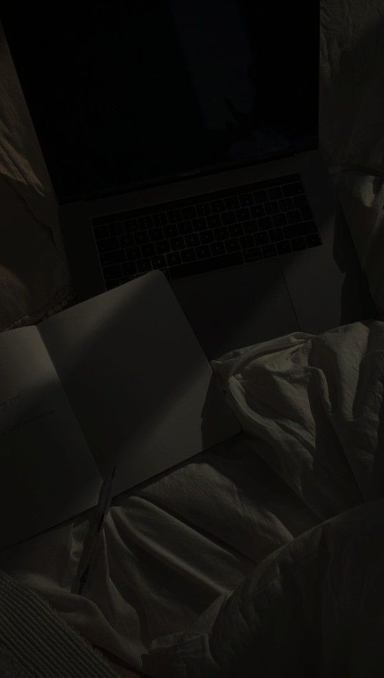 an open book sitting on top of a bed next to a laptop computer in the dark