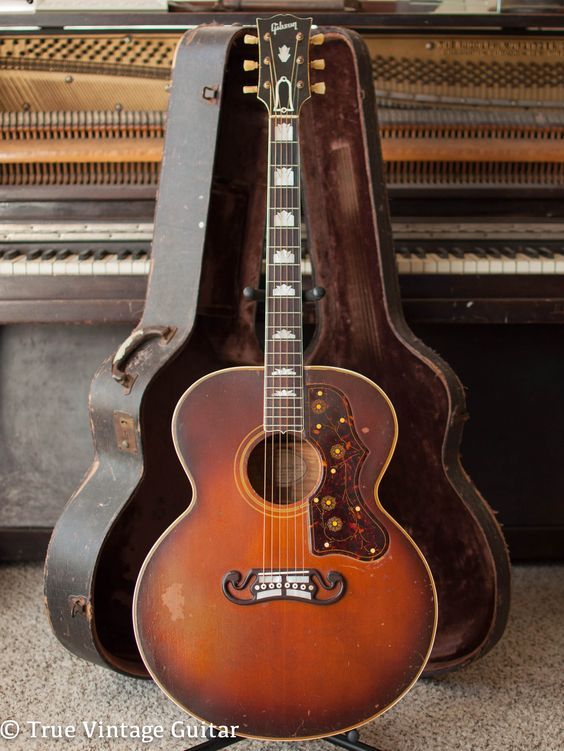 an old guitar sitting in front of a piano case with the top open and bottom closed