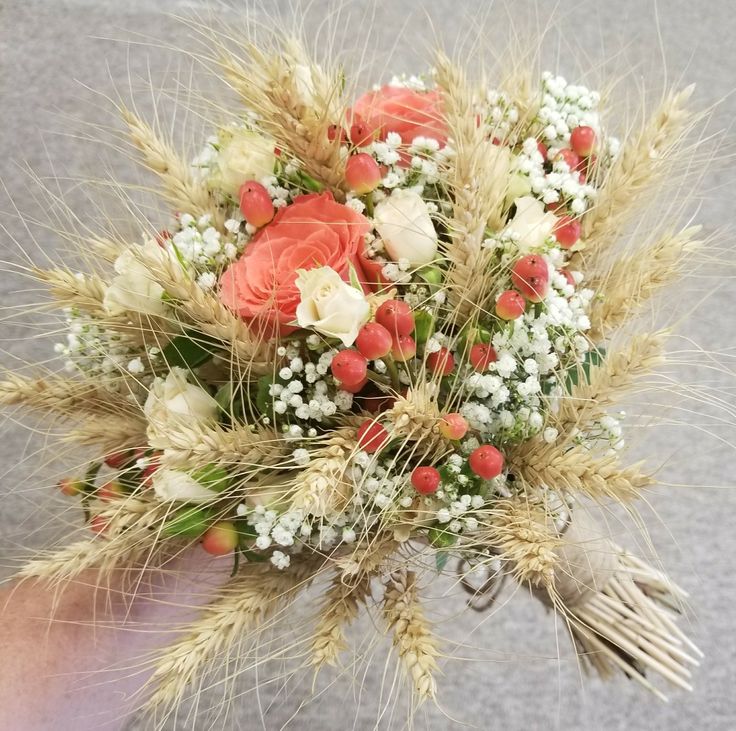 a person holding a bouquet of flowers and wheat stalks in their hand on the street