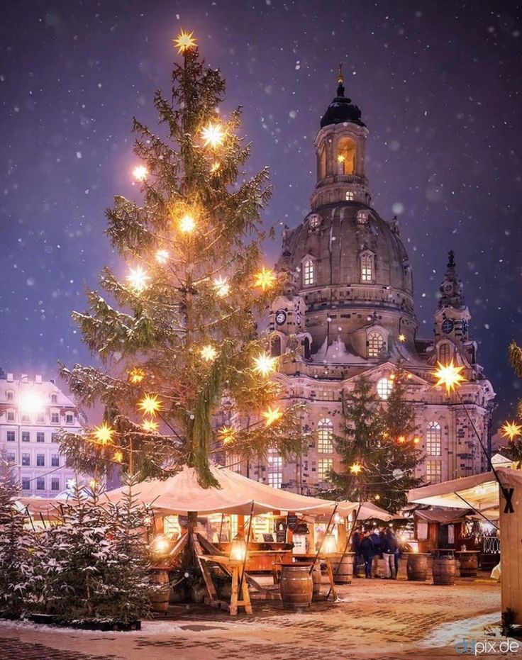 a christmas tree is lit up in front of a large building with many lights on it