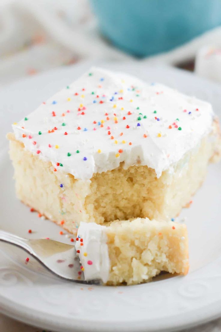 a piece of cake with white frosting and sprinkles is on a plate