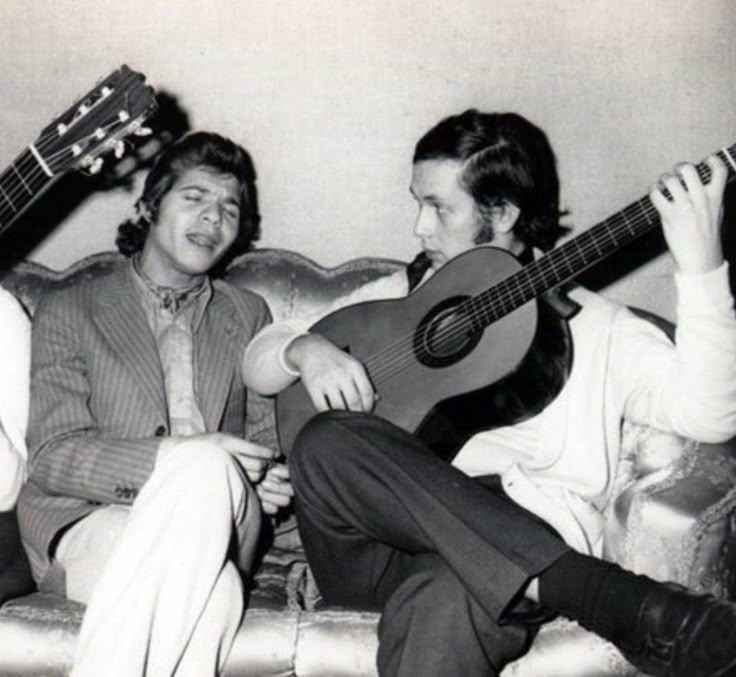 three men sitting on a couch with guitars in their hands and one playing the guitar