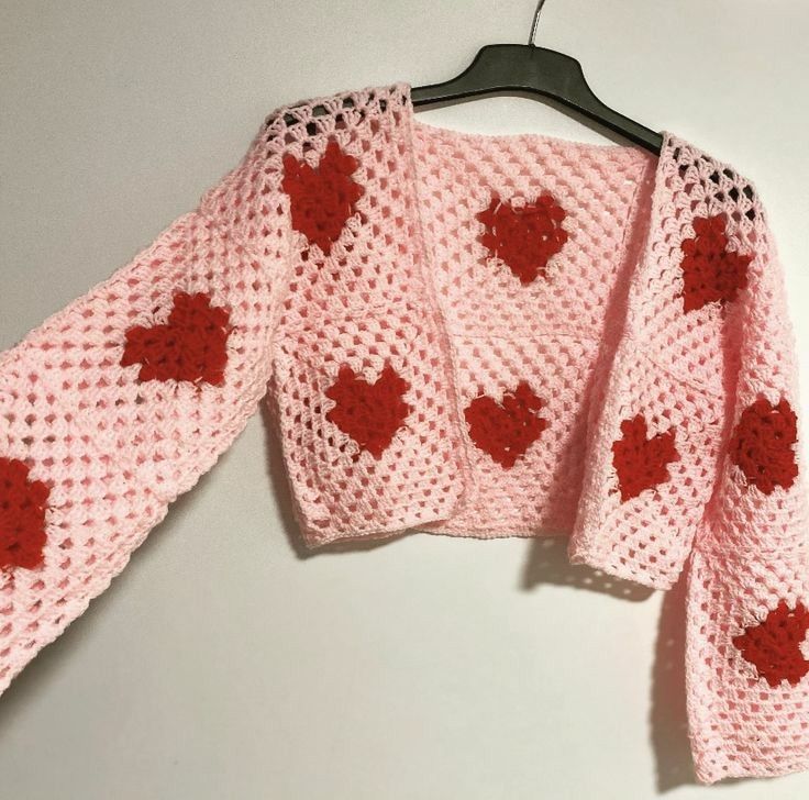 a pink knitted sweater with red hearts on the front and back, hanging from a hanger